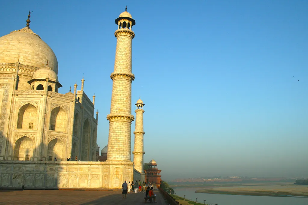 Taj Mahal river view from Yamuna bank in Agra, India – side angle of white marble mausoleum and tall minaret at golden hour